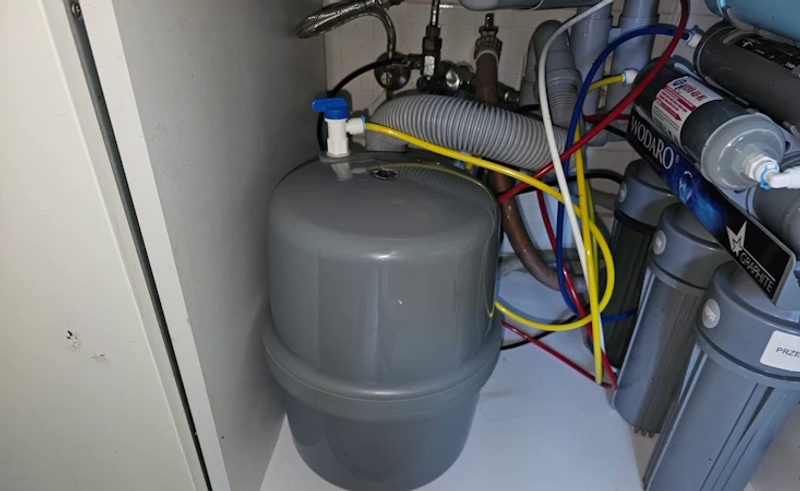 Zestaw filtra odwróconej osmozy w szafce pod zlewozmywakiem – szary zbiornik ciśnieniowy z zaworkiem i bateria filtrów obok